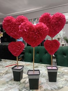 three heart shaped paper flowers in black planters on a table with green velvet chairs