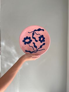 a hand holding a pink and blue plate with flowers on it's side, in front of a white wall