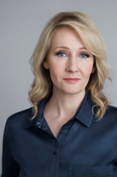 a woman with blonde hair and blue shirt posing for a photo in front of a gray background