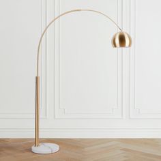 a floor lamp with a marble base and gold colored shade on the top, standing in front of a white wall