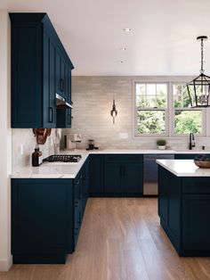 a kitchen with dark blue cabinets and white counter tops, wood flooring and an island