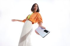 a woman in an orange shirt is holding a white and black electronic scale