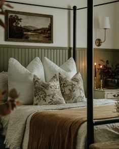 a bed with white and brown pillows in a bedroom next to a painting on the wall