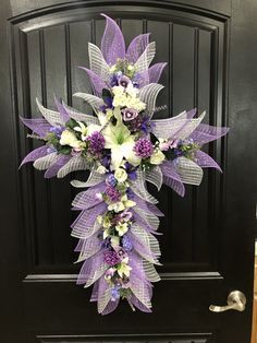 a cross made out of purple and white flowers on a black door with an iron handle