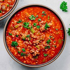 two bowls filled with beans and vegetables on top of a white table next to parsley