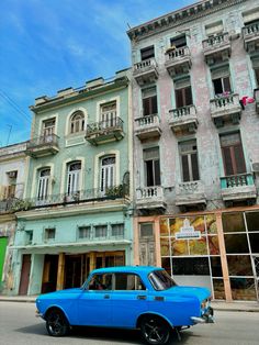 an old blue car is parked in front of some older buildings on the side of the road