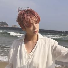 a man with pink hair standing in front of the ocean