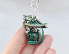 a hand holding a small green pendant with a fish on it's back,