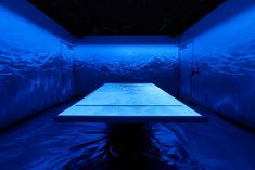 an empty room with blue lighting in the center and water on the floor at the bottom