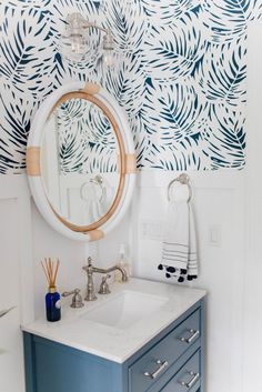 a bathroom sink with a mirror above it and palm leaves on the wall behind it