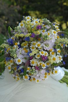 a bouquet of wildflowers and daisies on a white table cloth with greenery in the background