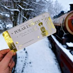 a person holding up a ticket to a train on the tracks in front of snow covered trees