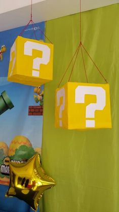 two yellow boxes with question marks hanging from them on a green wall next to a star shaped balloon