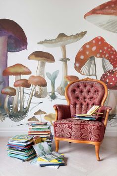 a chair sitting in front of a wall with mushrooms painted on it and books stacked next to it