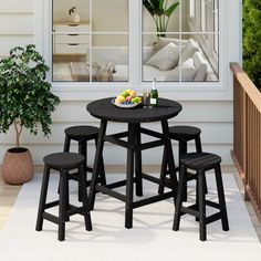 an outdoor table with four stools and a bowl of fruit on it in front of a window