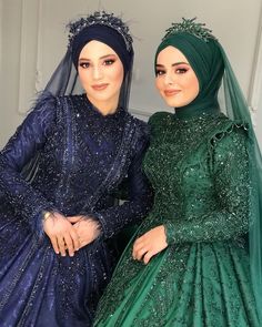 two women dressed in green and blue are posing for the camera, both wearing head coverings