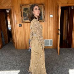 a woman standing in front of a wooden wall wearing a long dress with sequins on it