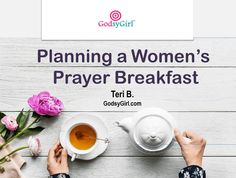 a woman's hands holding a cup of tea next to a white plate with pink flowers