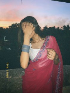 a woman in a red sari is covering her face with her hands and looking into the distance