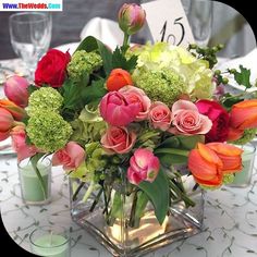 a vase filled with lots of colorful flowers on top of a white tablecloth covered table