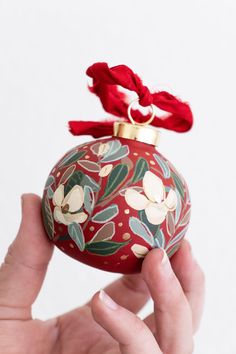 a hand holding a red ornament with flowers on it and a red ribbon