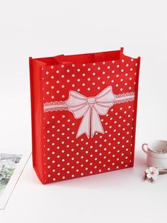 a red shopping bag with white polka dots and a bow on the front, sitting next to a coffee cup