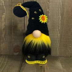 a black and yellow stuffed animal with a sunflower on it's head, sitting against a wooden wall