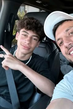 two men sitting in the back seat of a car, one pointing at the camera