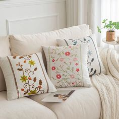 a white couch with pillows on top of it next to a table and potted plant