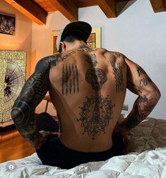 a man with tattoos on his back sitting on a bed