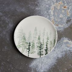 a plate with trees painted on it sitting on a concrete floor next to a wall