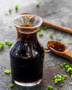 a glass bottle filled with black liquid next to a wooden spoon and sprigs of green leaves