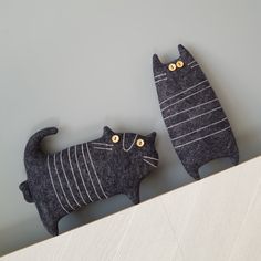 two black cats made out of felt sitting on top of a shelf next to each other