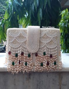 This is a beautiful handcrafted clutch bag made with love.It has intricate handwork which showcases the Indian craftsmanship by our local artisans. It comes with a pearl handle. Details  - Single side handwork  - Fabric lining on the inside to keep your belongings safe  - Magnetic lock closure  - Detachable handle  This clutch can be worn as a crossbody bag or a shoulder bag with the sling chain or can simply be carried in hand.It is spacious enough to carry mobile phones, lipsticks, Keys and ot Luxury Shoulder Bag With Pearl Handle As A Gift, Pearl Handle Clutch As Gift, Luxury Pouch Flap Bag With Detachable Handle, Luxury White Flap Bag As A Gift, Rectangular Evening Bag With Pearl Embroidery For Gift, Rectangular Pearl Embroidery Evening Bag As Gift, Rectangular Pearl Embroidery Evening Bag, Handmade Cream Evening Bag As Gift, Handmade Cream Evening Bag For Gift