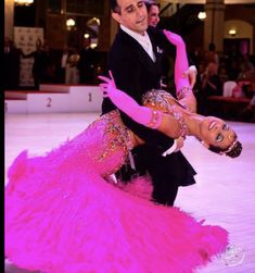 a man and woman in ballroom clothes on the dance floor with pink feathers around them