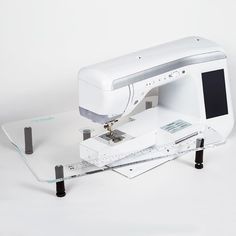 an electronic sewing machine sitting on top of a white table next to a computer monitor