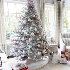 a white christmas tree with silver and red ornaments in a living room decorated for the holidays