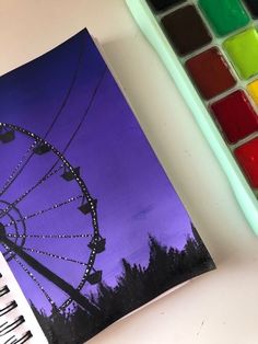 a painting of a ferris wheel with watercolors next to it and a paintbrush