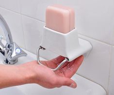 a person holding a soap dispenser in their hand over a sink faucet