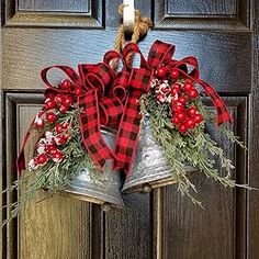 two bells with red and black plaid bows hang from the front door, decorated with greenery