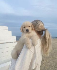 a woman holding a puppy on top of her back at the beach in front of the ocean