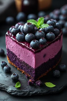 a piece of cake with blueberries and mint leaves on the top is sitting on a black plate