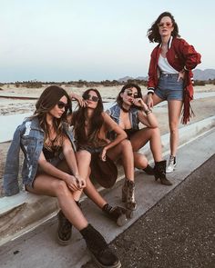 four young women sitting on the side of a road wearing short shorts and high heeled boots