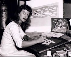 a black and white photo of a woman sitting at a desk working on some artwork