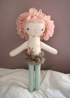 a doll with pink hair is standing on a bed