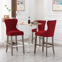 two red chairs sitting next to each other in front of a white table and wall