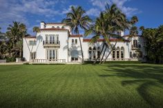 a large white house sitting on top of a lush green field next to palm trees