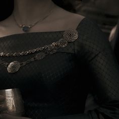 a woman in a black dress holding a cup and wearing a silver chain around her neck