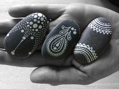 three black and white painted rocks in the palm of someone's hand, with paisley designs on them