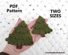 two crocheted christmas trees are in the palm of someone's left hand